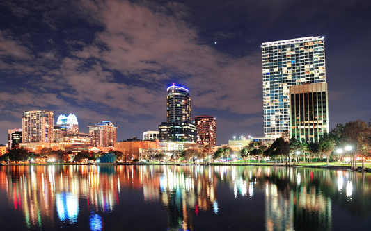 Nighttime city skyline with illuminated high-rise buildings reflecting in a calm lake
