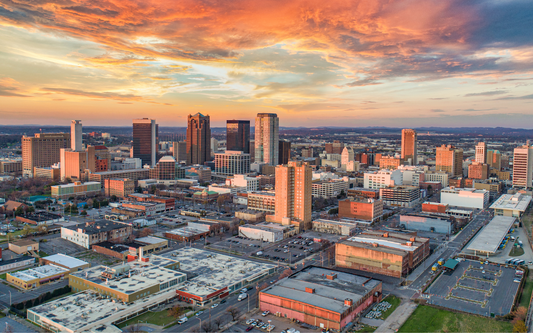 Aerial view of a city skyline at sunset with warm orange and purple clouds