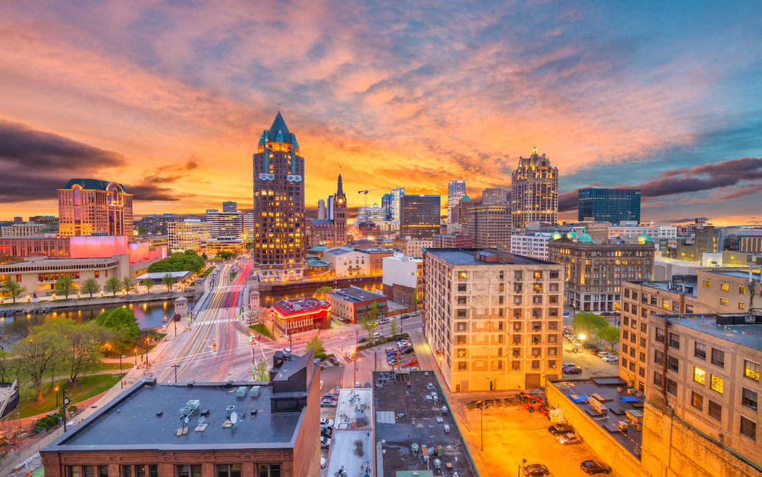 Downtown skyline at sunset with illuminated buildings, riverfront, and traffic light trails on city streets