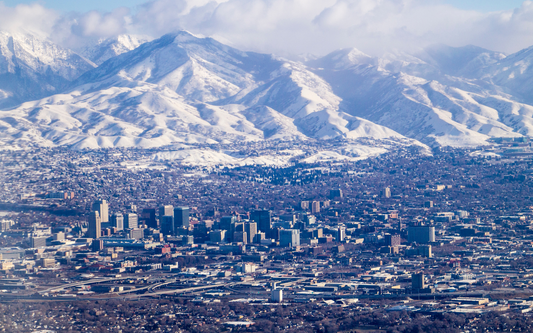 Aerial view of a Utah city skyline with snow‑covered mountains rising behind it