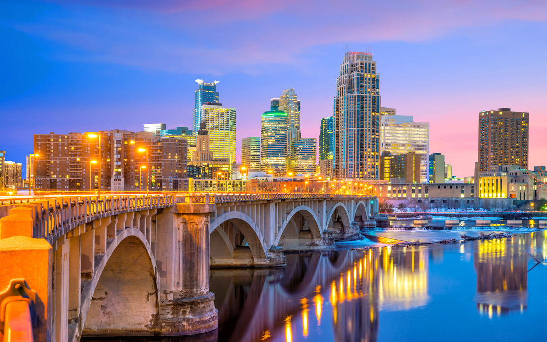 Arched bridge leading to downtown Minneapolis skyline at dusk with city lights reflecting in the river