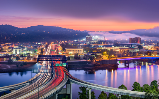 Highway bridge with vehicle light trails leading into a West Virginia riverfront city at sunset