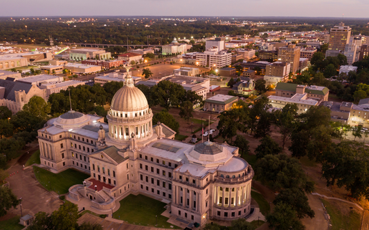 Aerial view of the Mississippi State Capitol building at dusk with downtown Jackson visible in the background