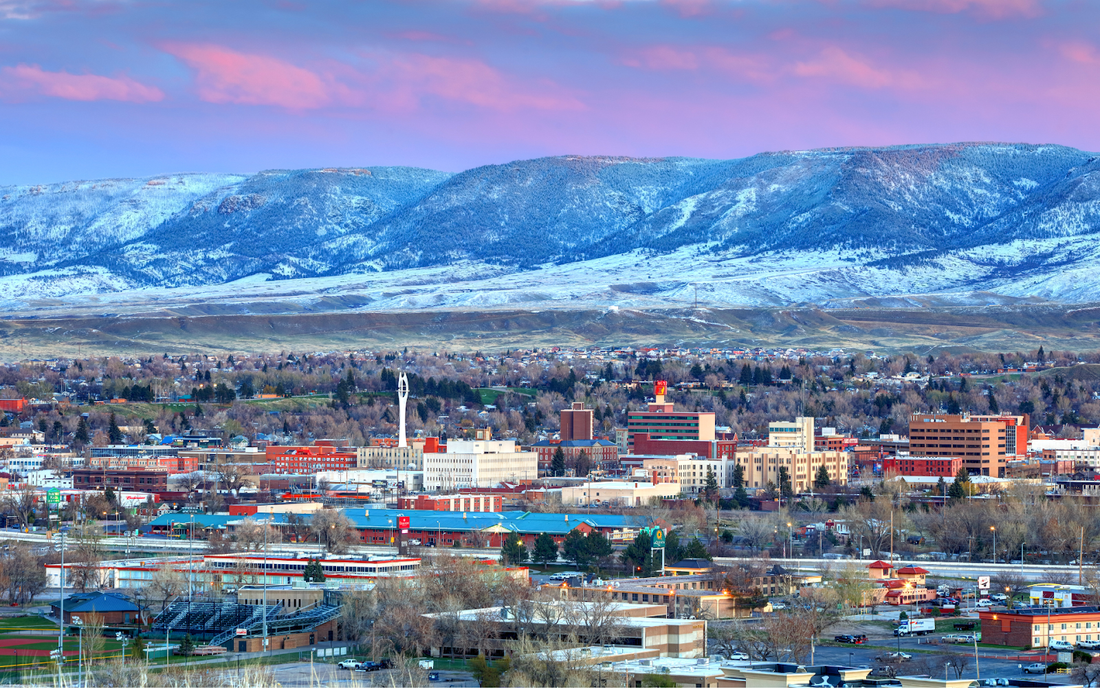 Wyoming city skyline at sunrise with downtown buildings in the foreground and snow-dusted mountains under a pink sky