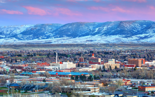 Wyoming city skyline at sunrise with downtown buildings in the foreground and snow-dusted mountains under a pink sky