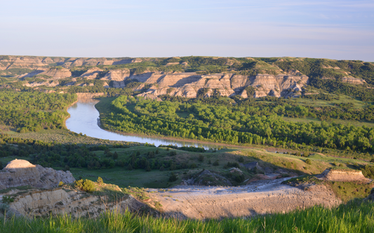 Missouri River winding through a green valley and layered sandstone badlands in North Dakota at golden hour
