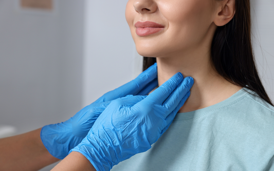 Healthcare provider in blue gloves palpating a woman’s neck during a thyroid exam in a clinic