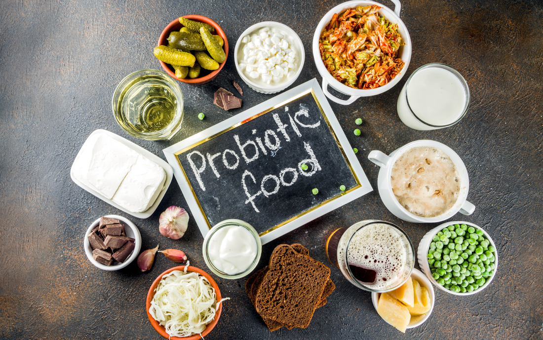 Assortment of probiotic foods arranged around a chalkboard that reads Probiotic food on a dark tabletop