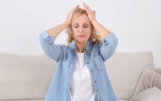 Woman holding her head with both hands on a couch, eyes closed and appearing to have a headache