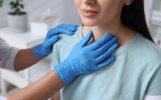 Clinician wearing blue gloves palpates a woman’s neck during a thyroid exam in a clinic setting