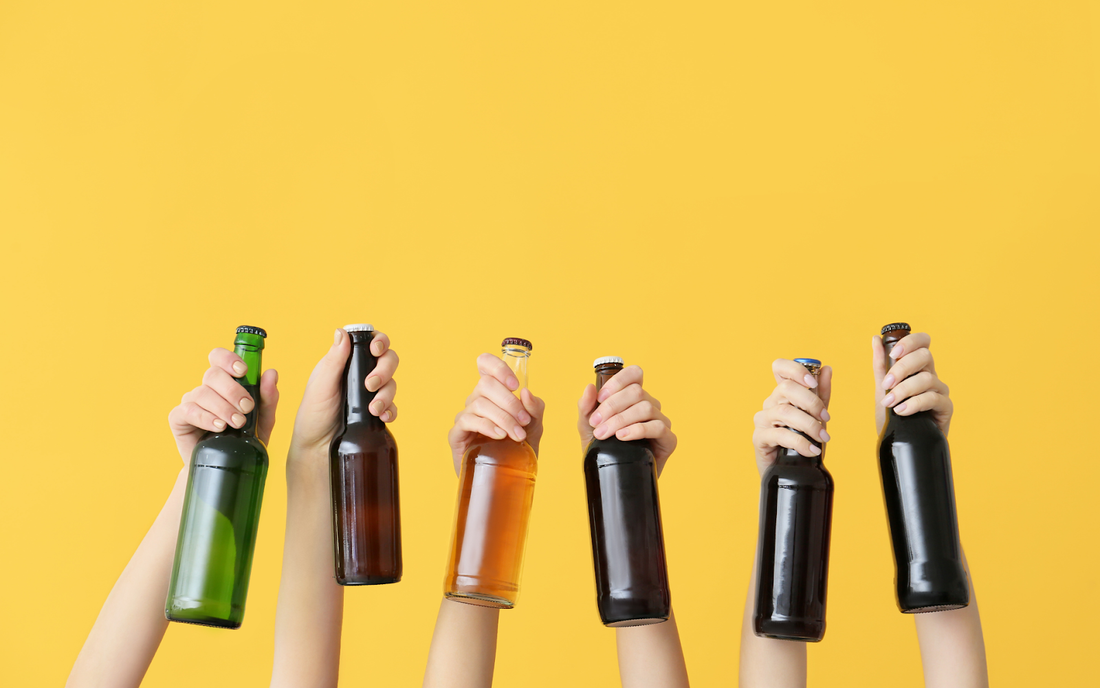 Several hands holding up beer bottles against a bright yellow background