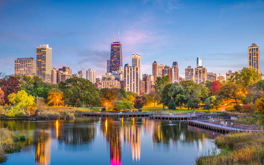 Chicago skyline at dusk reflected in a park pond with autumn trees and a wooden boardwalk