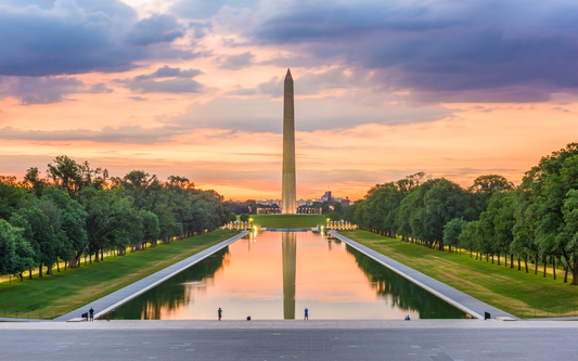 Washington Monument reflected in the Lincoln Memorial Reflecting Pool at sunset with orange-pink sky and tree-lined lawns