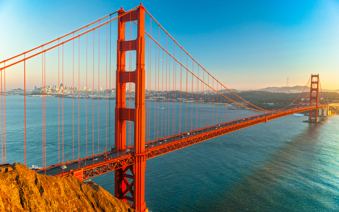 Golden Gate Bridge spanning San Francisco Bay at golden-hour light with the San Francisco skyline in the background