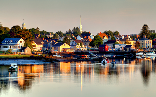 Small boats moored in a New Hampshire harbor with colorful waterfront houses and a white church steeple at sunrise