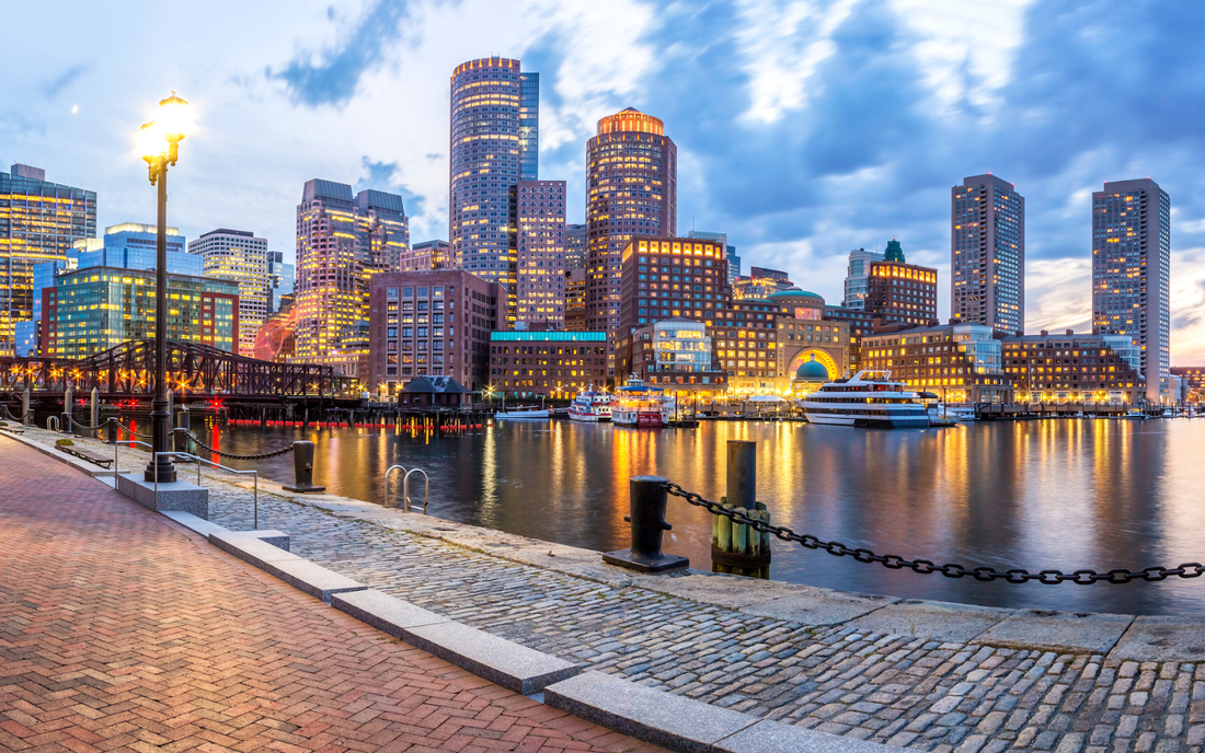 Dusk view of Boston skyline along the harbor, waterfront promenade and buildings lit with reflections in the water
