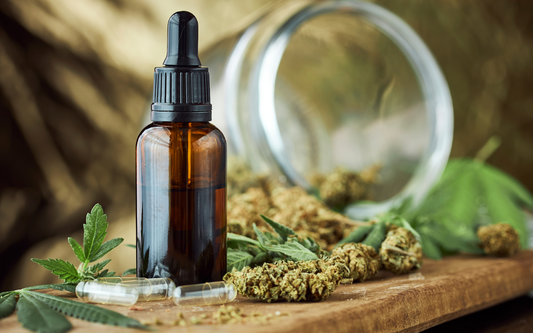 Amber glass dropper bottle sitting on a wooden board with cannabis buds, hemp leaves, and empty capsules in soft-focus background