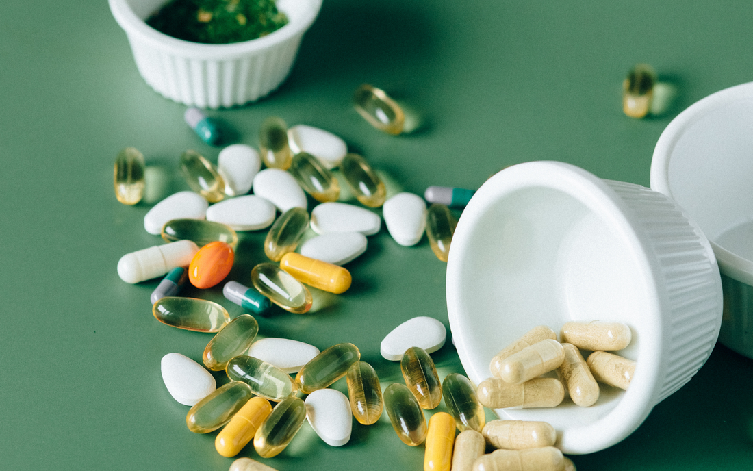 Various supplement capsules and tablets spilled from a white container onto a green surface