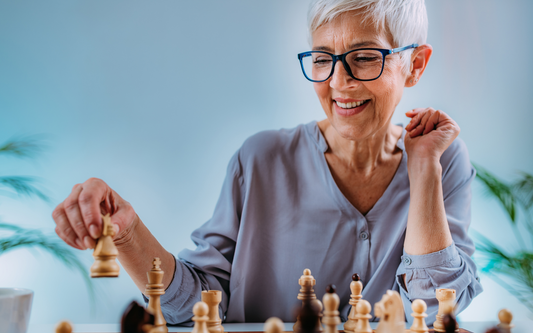 Older woman smiling while moving a chess piece on a chessboard in a bright room