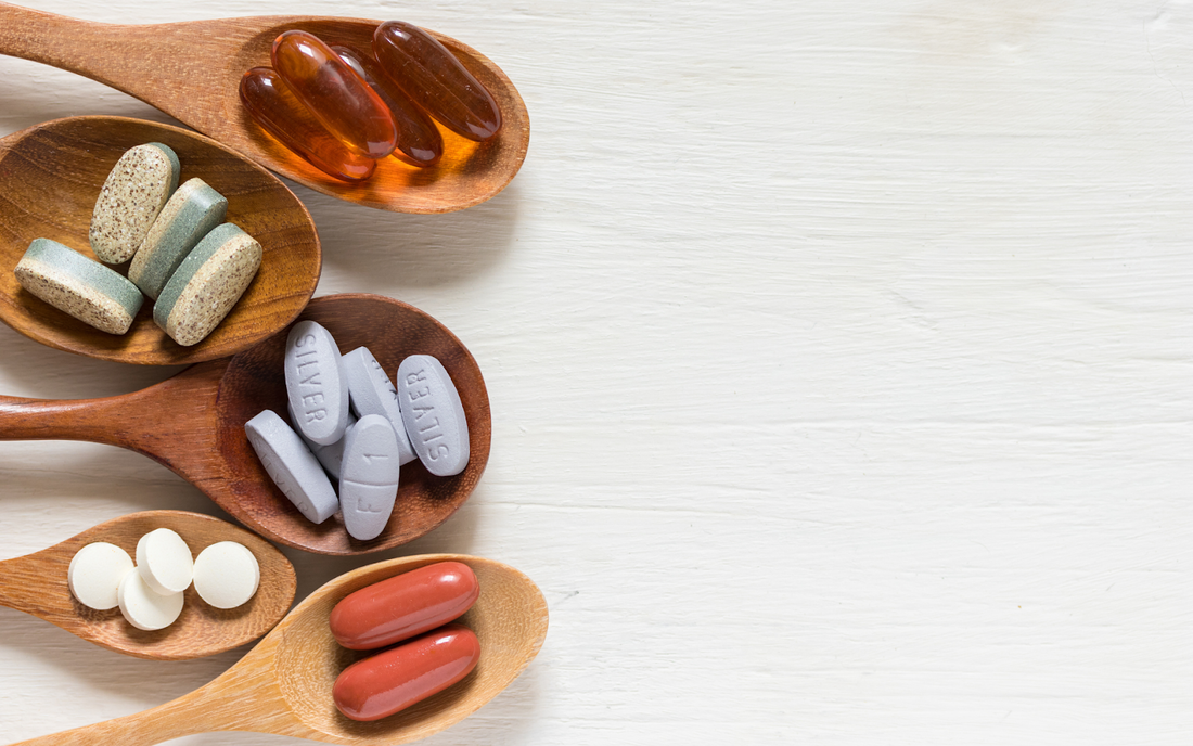 Several wooden spoons holding assorted supplement pills and capsules on a white wooden background