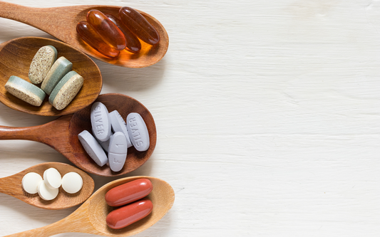 Several wooden spoons holding assorted supplement pills and capsules on a white wooden background