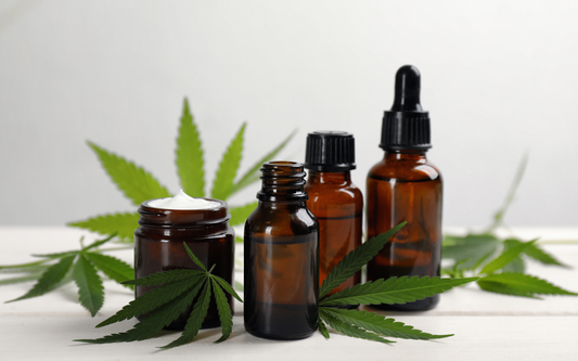 Amber dropper bottles and a cream jar displayed with cannabis leaves on a white tabletop