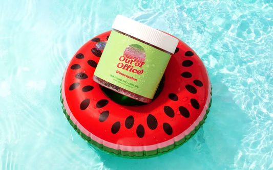Angled front view of Out of Office Watermelon gummies jar with white lid and droplets on a watermelon pool float in a pool