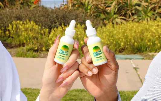 Two people holding Out of Office pineapple hemp oil dropper bottles outdoors in a sunny park setting