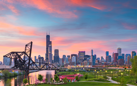 Chicago skyline at sunset with an open industrial drawbridge and lit riverside park in the foreground