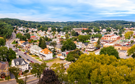 Aerial view of a New Jersey small town with tree-lined streets, detached houses, and a distant wooded hillside