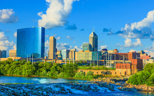 Indianapolis skyline over the White River at golden hour with downtown skyscrapers and a leafy riverbank