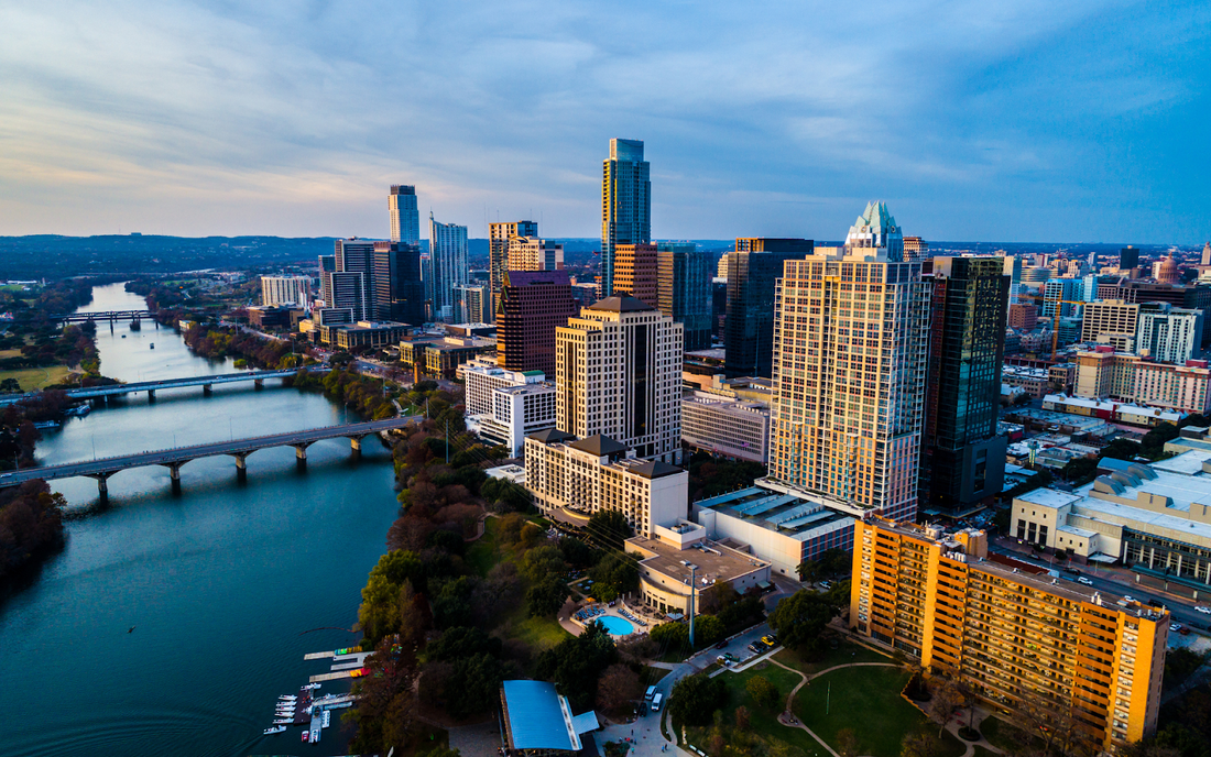 Aerial view of downtown Austin skyline along the Colorado River at dusk, showing bridges and high-rise buildings