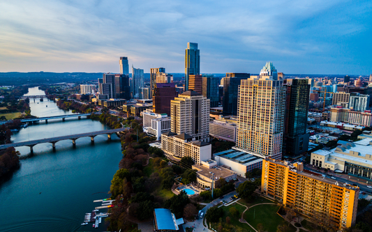 Aerial view of downtown Austin skyline along the Colorado River at dusk, showing bridges and high-rise buildings