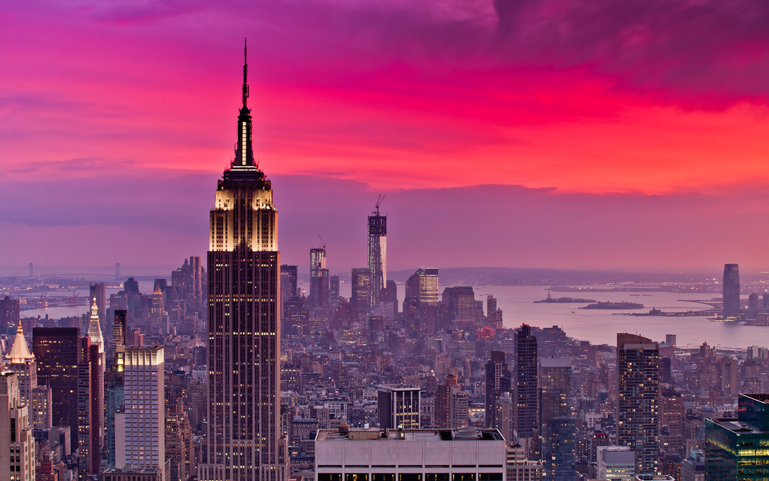 Empire State Building rising above the Manhattan skyline at sunset with pink and purple sky