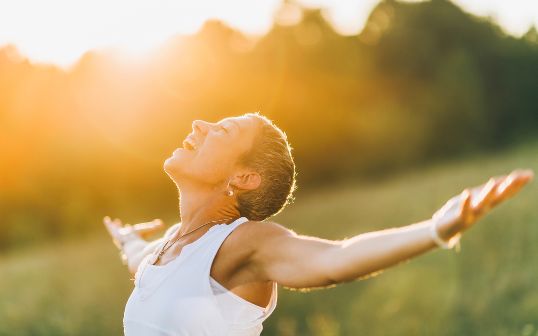 Person smiling with arms outstretched in a sunlit field at golden hour