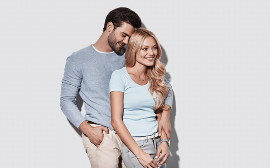 Smiling couple embracing, man standing behind woman against a light gray background