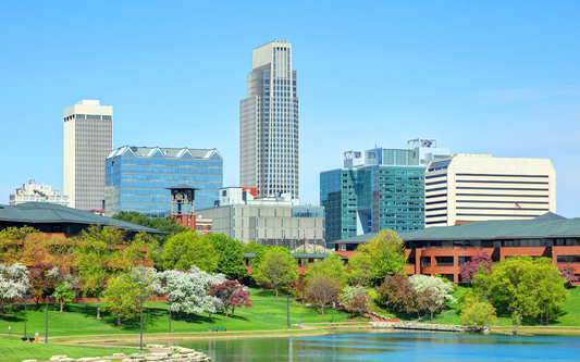 Downtown skyline rising behind a green park and reflective pond on a sunny, clear day