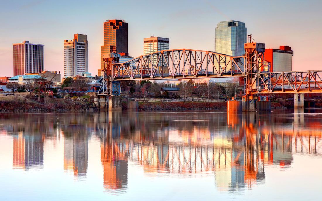 Little Rock skyline at sunset with downtown skyscrapers and a steel lift bridge reflected in the Arkansas River
