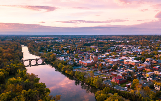Aerial view of a riverside Virginia town at sunset with a three-arch stone bridge over the river and tree-lined banks