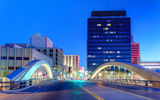 Arched concrete bridge leading into a downtown city skyline at twilight with illuminated office windows