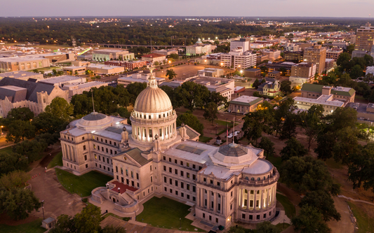 Aerial view of the Mississippi State Capitol building at dusk with the Jackson city skyline in the background