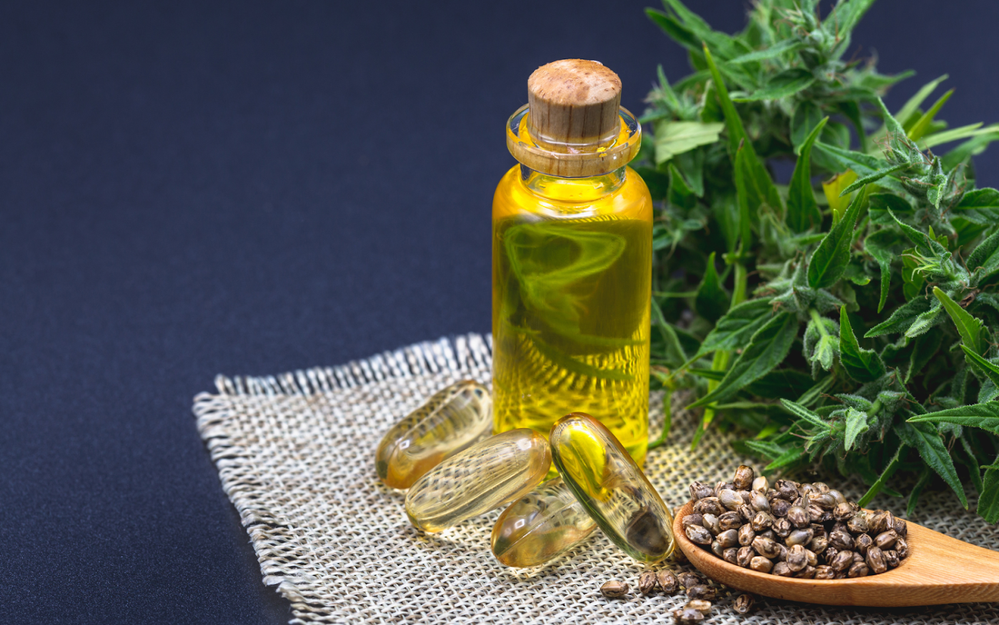 CBD oil bottle and softgel capsules beside hemp seeds and cannabis leaves on burlap against dark background