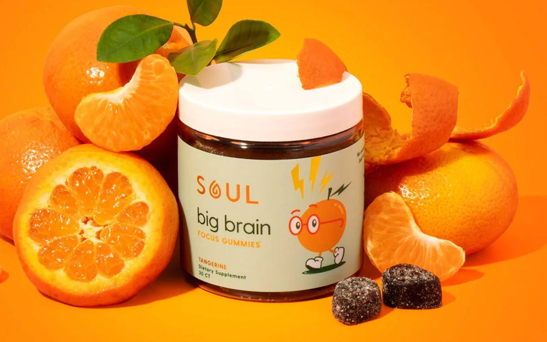 Front view of Soul Big Brain Focus Gummies jar with tangerine label, sliced tangerines and two gummies on orange background