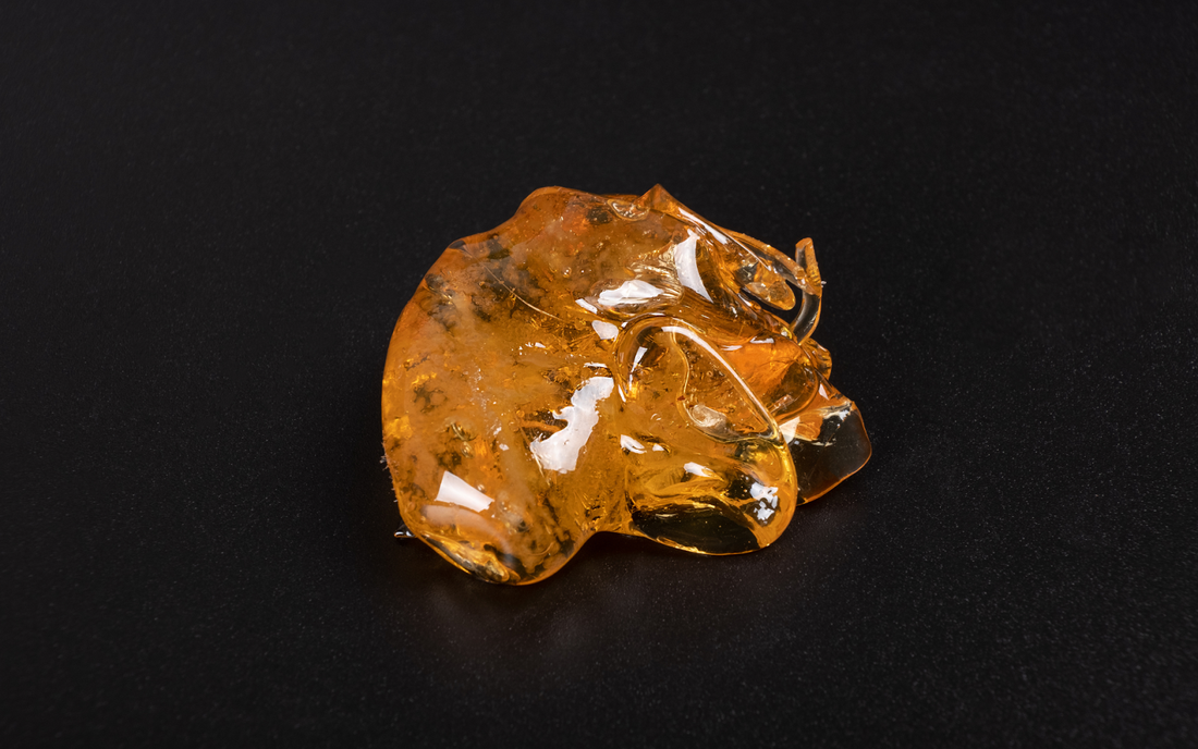 Top view of amber cannabis concentrate (shatter) showcasing glossy translucent texture on a black background