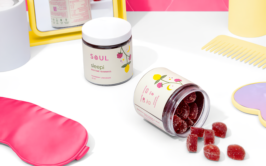 Angled overhead view of Soul Sleepi gummy jars, one open with red sugar‑coated gummies spilled onto a white surface