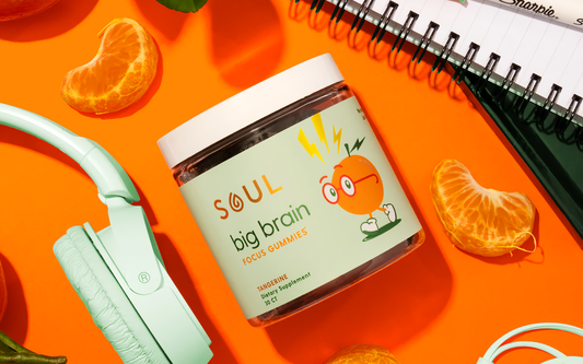 Angled flatlay of Soul Big Brain gummies jar showing Tangerine label on orange background with headphones and tangerine slices