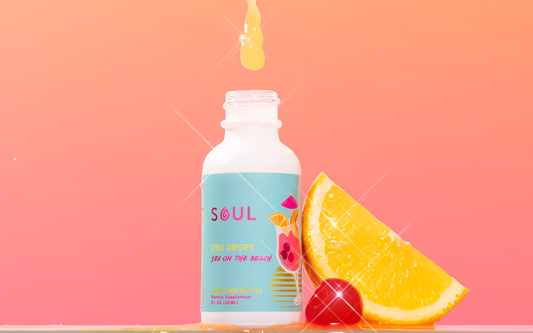 Front of Soul CBD Drops bottle labeled Sex on the Beach with droplet above and orange wedge and cherry on pink background
