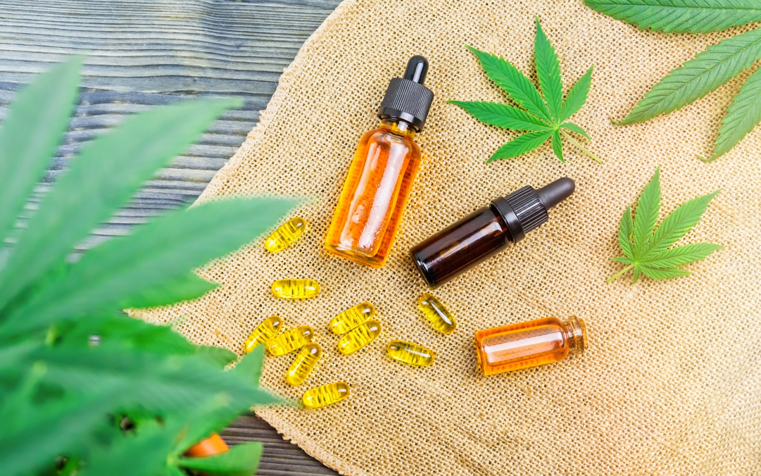 Bottles of CBD oil and softgel capsules arranged on burlap with hemp leaves