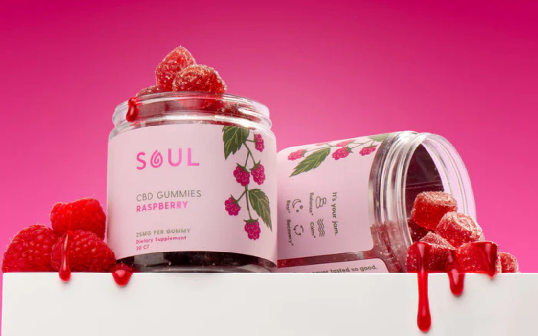 Three-quarter view of Soul Raspberry CBD gummies jar showcasing label and sugar-coated gummies spilling with a pink gradient background