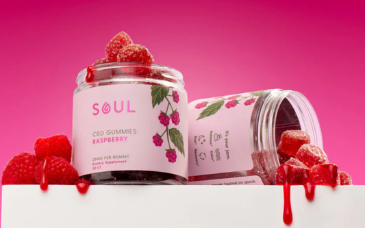Three-quarter view of Soul Raspberry CBD gummies jar showcasing label and sugar-coated gummies spilling with a pink gradient background